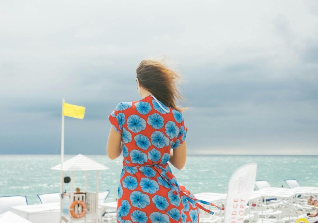 Back view of a woman in a vibrant floral dress standing on a Sochi beachfront.