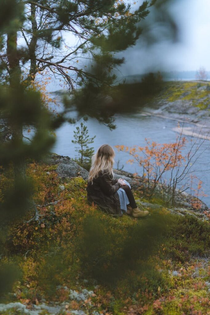 A woman enjoys a peaceful moment by the autumn lakeside, surrounded by nature.