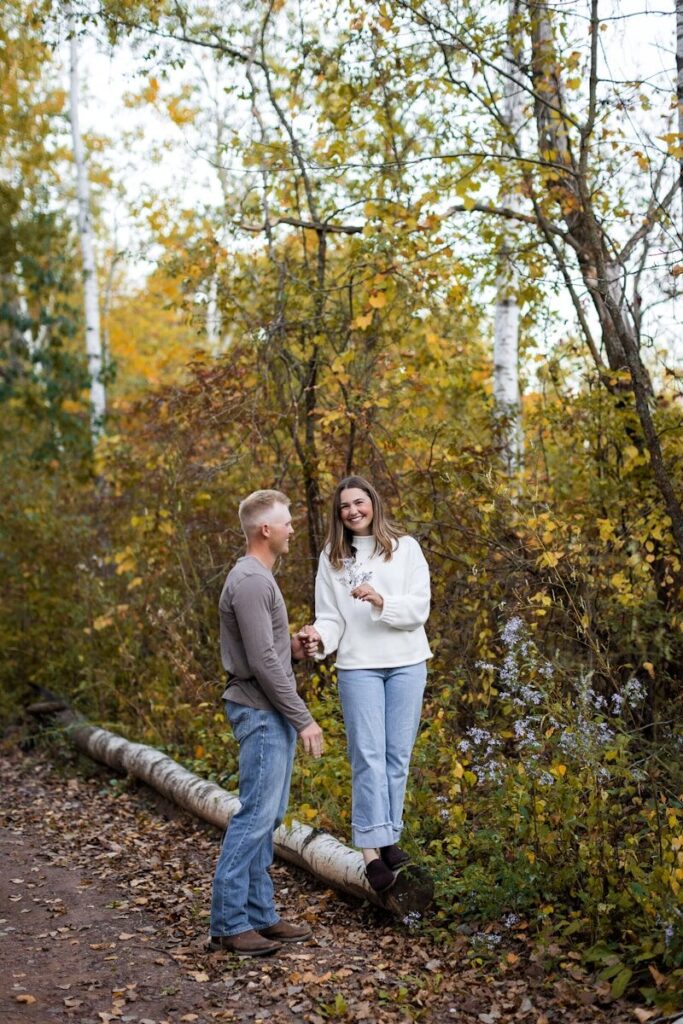 Couple standing on a fallen tree trunk in autumn woods.